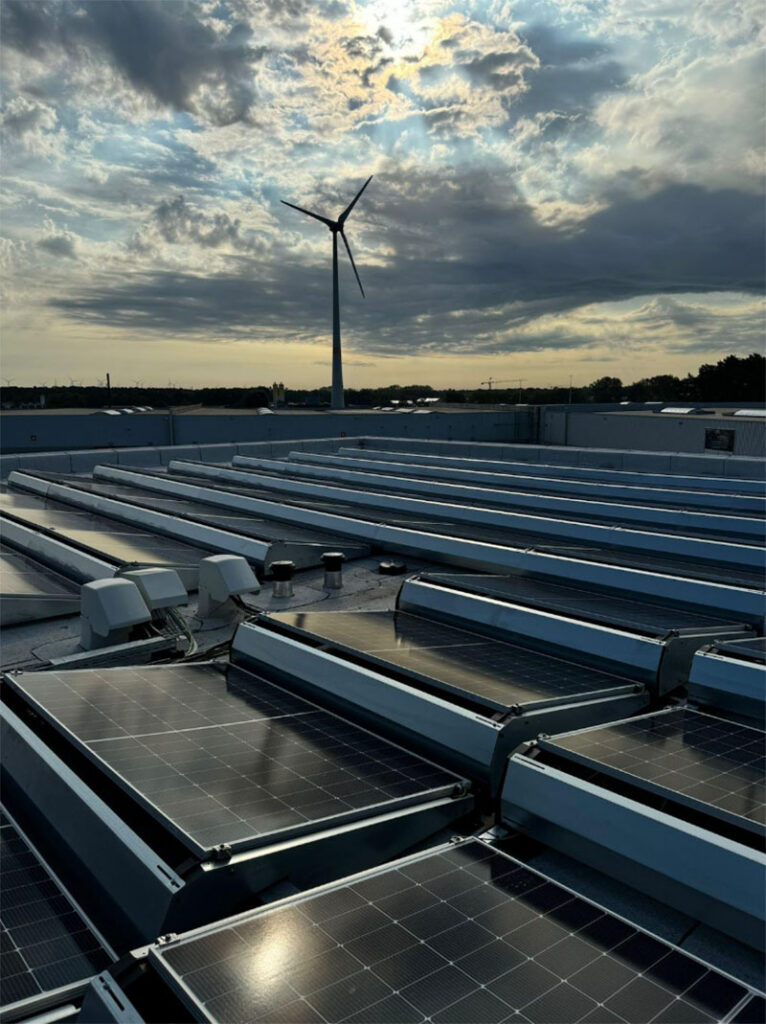 Zonnepanelen op het dak van Gheys HQ met zicht op windturbine bij zonsondergang als onderdeel van duurzame energieoplossingen.